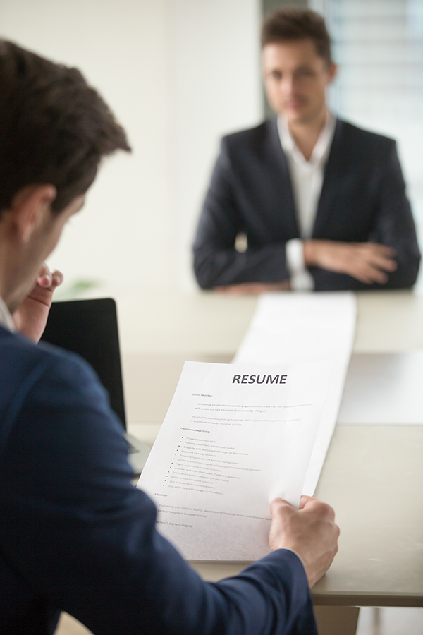 Back view of employer reading resume focus on document, job applicant waiting for hiring decision at desk on background. Hiring manager studying long list of candidates achievements and experiences